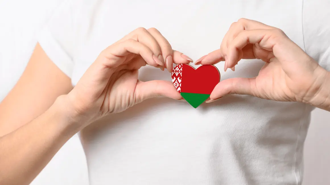 Zbliżenie na dłonie osoby w białej koszulce, trzymające serce w kolorach flagi Białorusi